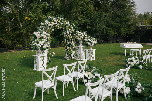 Wedding ceremony outdoor. A beautiful and stylish wedding arch, decorated by various fresh white flowers with white chairs, standing in the garden. Celebration day.