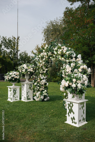 Wedding ceremony outdoor. A beautiful and stylish wedding arch, decorated by various fresh white flowers with white chairs, standing in the garden. Celebration day.