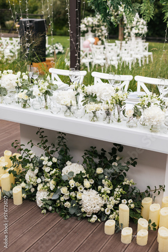 Wedding ceremony outdoor. Presidium for the newlyweds, decorated with candles and vases with white natural flowers such as eustoma, hydrangea, roses and eucalyptus
