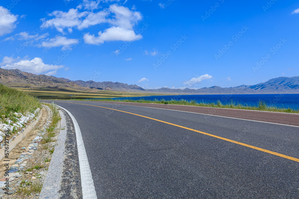 Asphalt road and lake with mountain natural scenery in Xinjiang, China.