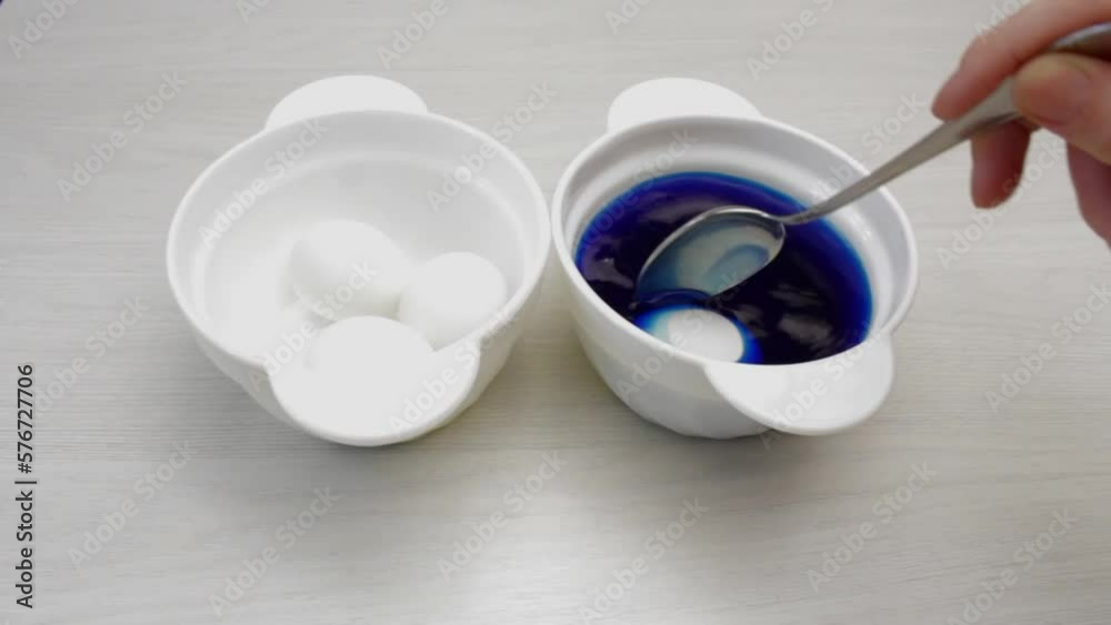 A woman paints Easter eggs with blue paint on a white table. Religion, easter concept. A woman paints Easter eggs with blue paint on a white table. Religion, easter concept.