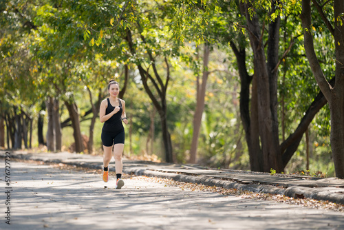 A young runner woman wearing fitness clothing runs in a city park surrounded by trees and greenery