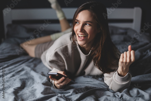 Wallpaper Mural Excited winner checking online the phone for a prize lying on the bed at home. Winning and triumphing. Excited girl in bed, looking at her phone with amazed, surprised face, celebrating victory. Torontodigital.ca