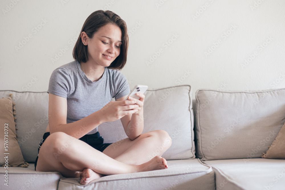 Content woman messaging via smartphone while lying on sofa Content woman messaging via smartphone while lying on sofa