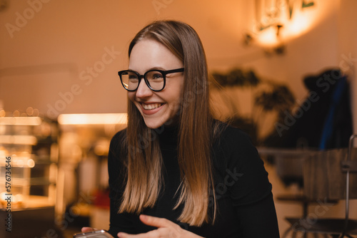Charming woman with beautiful smile reading good news on mobile phone during rest in coffee shop, happy Caucasian female watching her photos on cell telephone while relaxing in cafe during free time. © zvkate