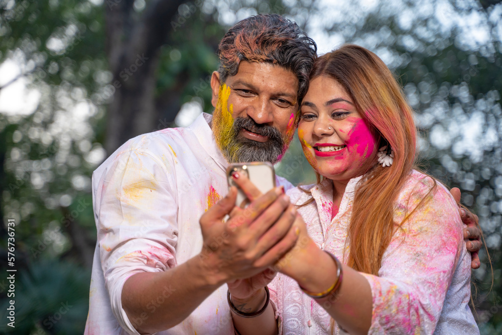 Fototapeta premium young indian couple looking at smartphone and playing holi