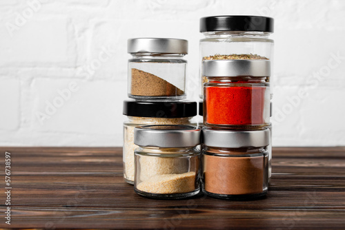 Bright fragrant spices in glass jars of different sizes on a wooden table. Proper storage of spices
