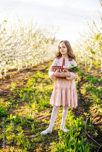 Beautiful caucasian blonde girl in a pink dress with a basket in the garden of flowering trees in spring. 