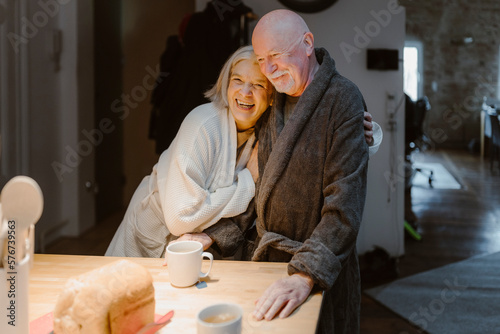 Happy senior woman embracing man wearing bathrobe at home photo