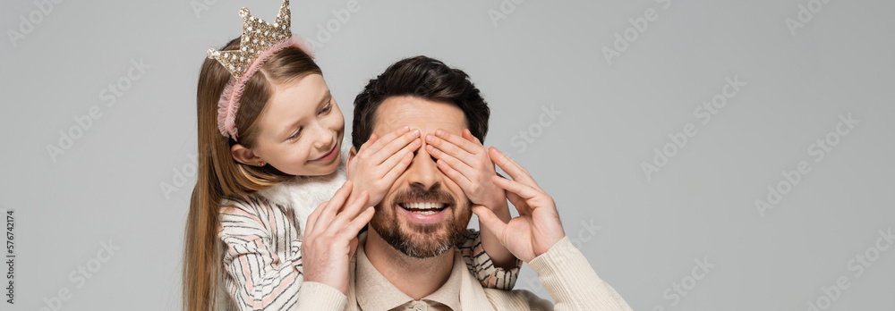 cheerful kid in crown covering eyes of bearded father isolated on grey, banner.