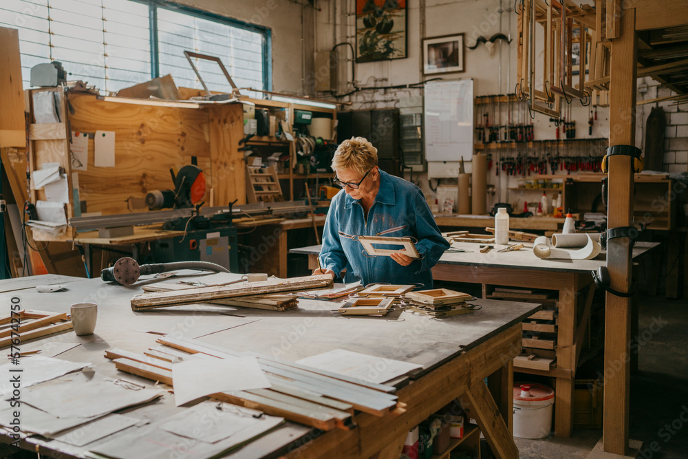 Senior female carpenter holding frame while working at workshop Senior female carpenter holding frame while working at workshop