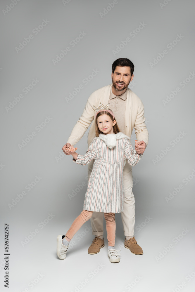 full length of smiling man in white outfit holding hands with happy daughter in grey. full length of smiling man in white outfit holding hands with happy daughter in grey.