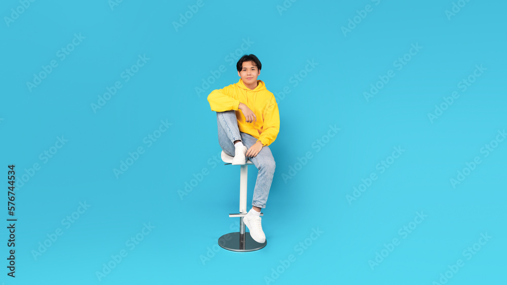 Korean Teenager Boy Sitting On Bar Stool Over Blue Background