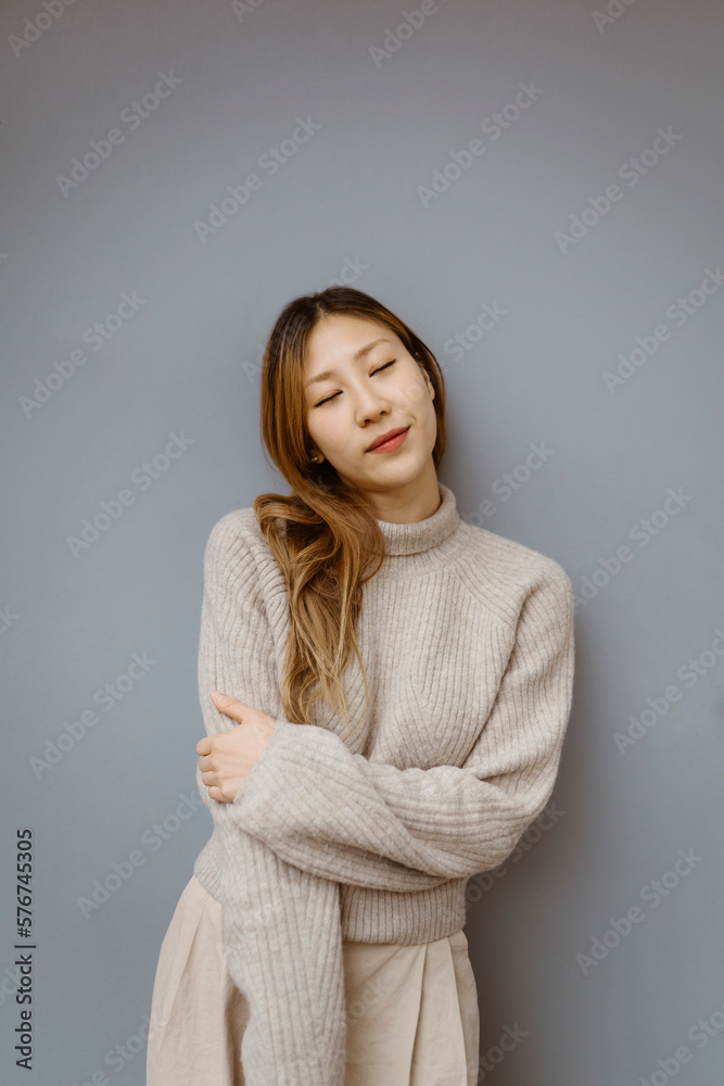 Young woman with eyes closed standing against gray background Young woman with eyes closed standing against gray background