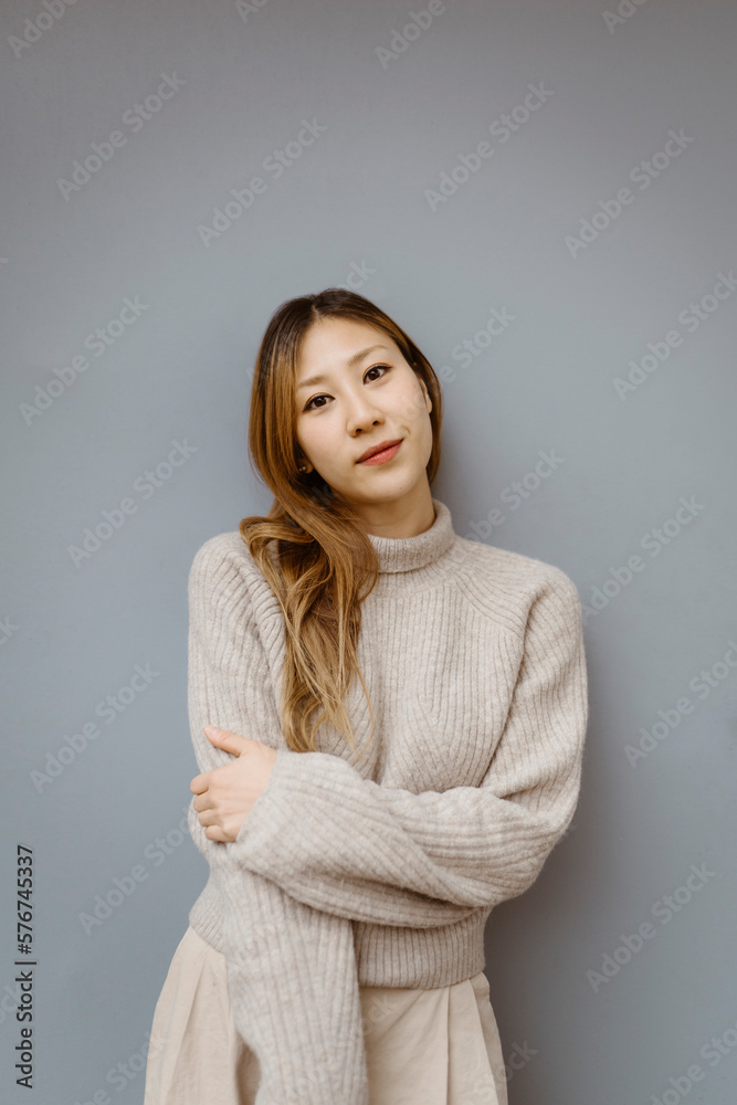 Portrait of young woman wearing sweater while standing against gray background Portrait of young woman wearing sweater while standing against gray background
