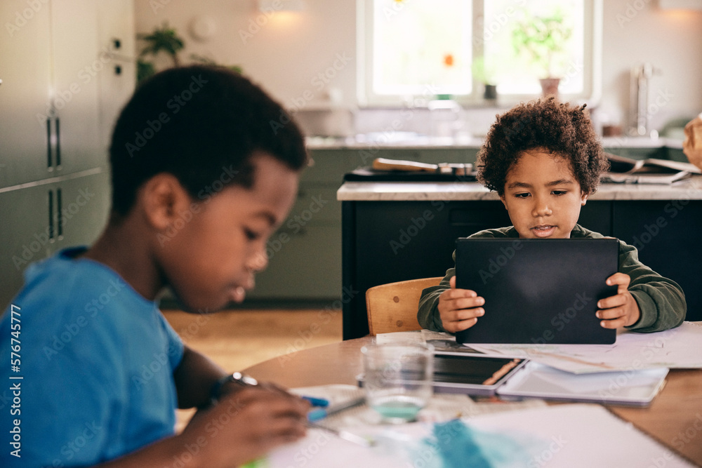Boy using digital tablet while brother coloring in book at home Boy using digital tablet while brother coloring in book at home