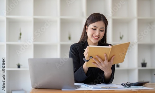 Focused Asian female accountant or financial analyst at laptop screen and taking notes