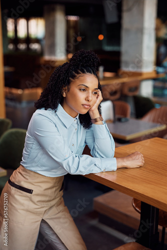 Young black waitress thinks of something while working in cafe and looking away.