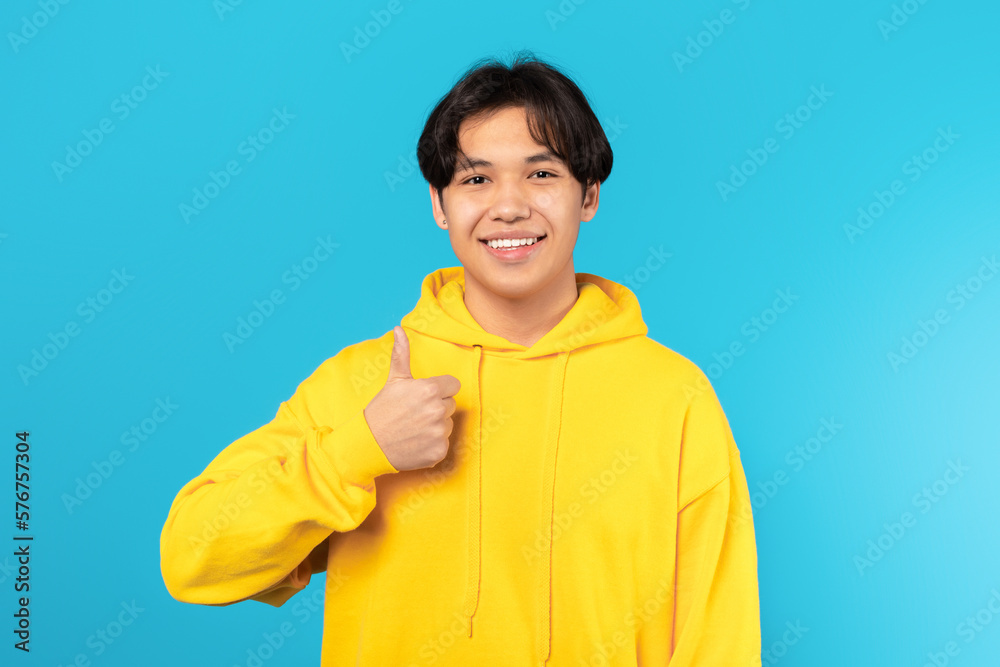 Happy Asian Teenager Guy Gesturing Thumbs Up On Blue Background Happy Asian Teenager Guy Gesturing Thumbs Up On Blue Background