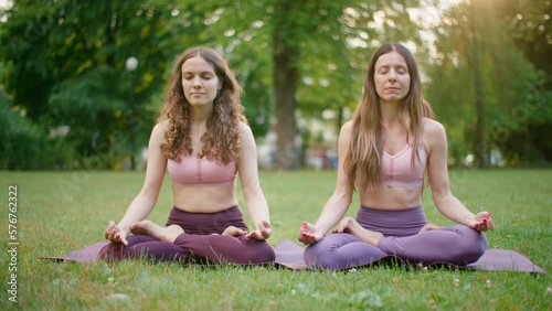 Two Sporty Women doing Meditaton in Park. Fit Ladies Stretch and do Sports outdoors in Lotus Poses. Mindfullness and Healthy Lifestyle and Meditation 4K wide orbit shot photo