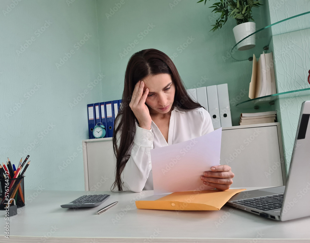 Unhappy woman touching forehead and holding paper reading bad negative news in letter at workplace Unhappy woman touching forehead and holding paper reading bad negative news in letter at workplace