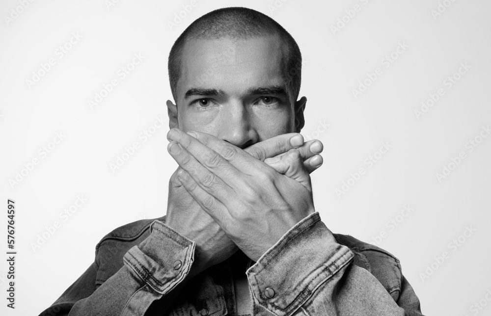Brutal guy covers his lip with his hands. Portrait of man with depressive emotion on gray background. Black and white photo. Brutal guy covers his lip with his hands. Portrait of man with depressive emotion on gray background. Black and white photo.