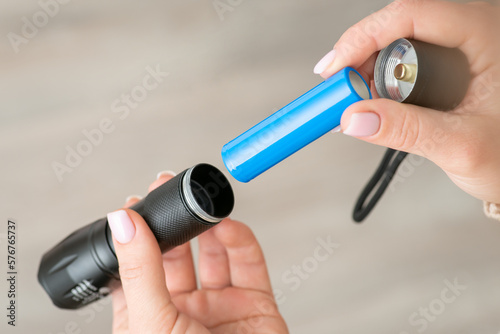 Black flashlight, female hands inserting blue 18650 battery in it, close up. Device for lightning, power for portable flashlight