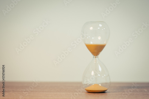 Sandglass standing on wooden table, white wall on the background, copy space. Sand timer, concept of time, speed, deadline, measurement, deadline. Toned photo