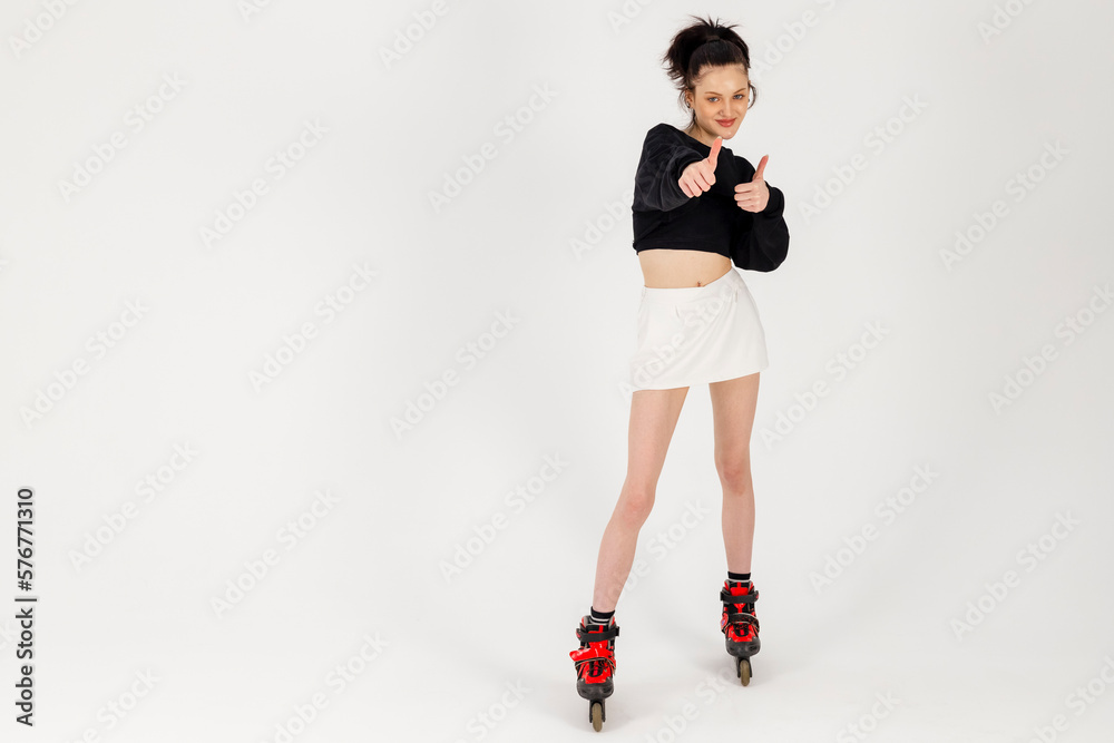 Attractive Slim Girl in black short top and white mini skirt wearing inline skates, showing thumbs up. Isolated on white background.