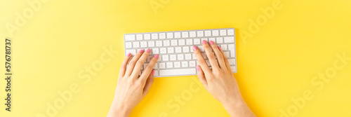 Woman’s hands working on computer with accessories on yellow background. Office desktop. Top view