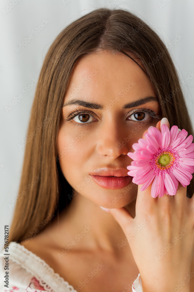 Portrait of young beautiful long-haired brown-eyed woman with pink gerbera on white background. Spring. Holidays. Mothers Day. Portrait of young beautiful long-haired brown-eyed woman with pink gerbera on white background. Spring. Holidays. Mothers Day.