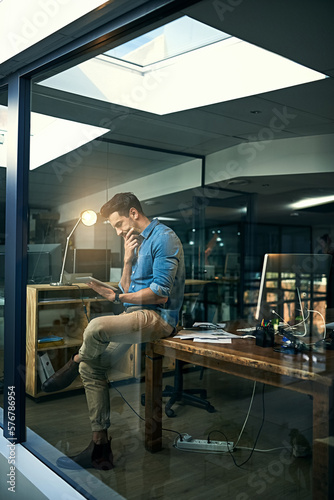 His motto - Its not done until its done. Shot of a young businessman using a digital tablet during a late night at work.