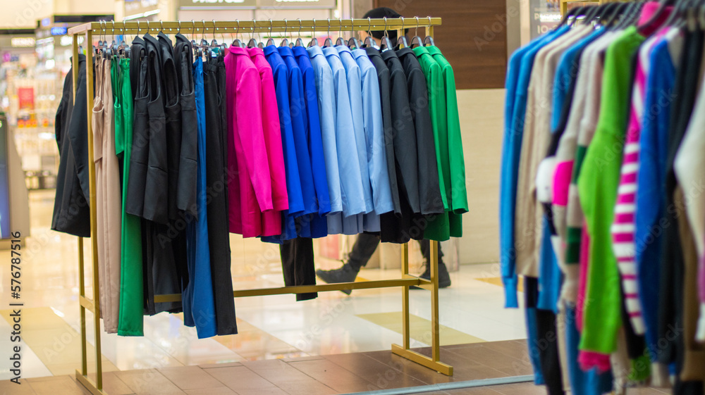 Rack of fashionable women's clothing, selective focus. Hangers in a row with bright women's clothing on a rail in the hall of a store in a shopping center. Shop for sale and fashion show.