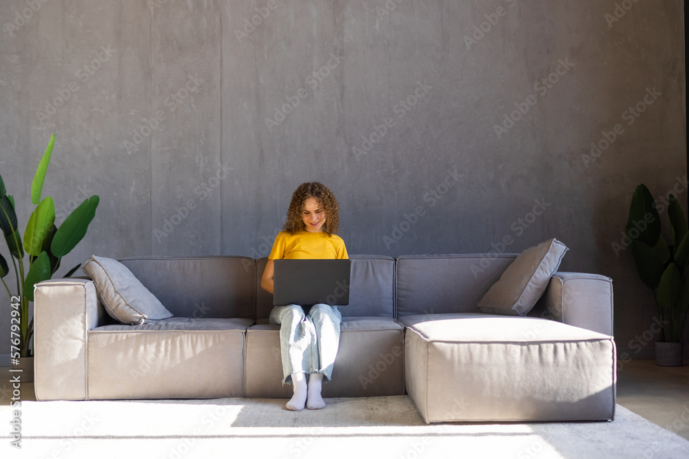 Obraz premium Photo of cnice woman smiling and using laptop while sitting on couch in bright room