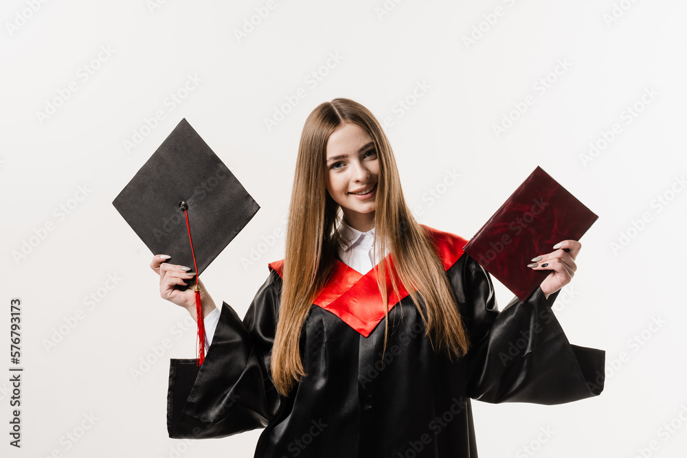 Graduate girl master degree in black graduation gown is holding diploma and cap in hands on white background. Attractive young woman graduated from college. Graduate girl master degree in black graduation gown is holding diploma and cap in hands on white background. Attractive young woman graduated from college.
