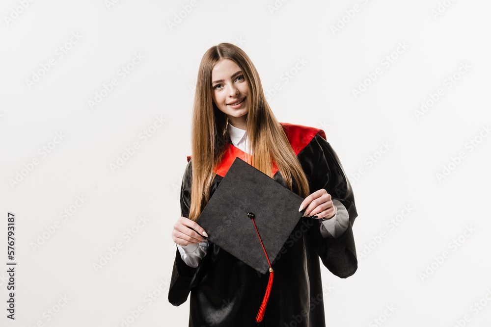 Graduate girl master degree in black graduation gown is holding cap in hands on white background. Attractive young woman graduated from college.