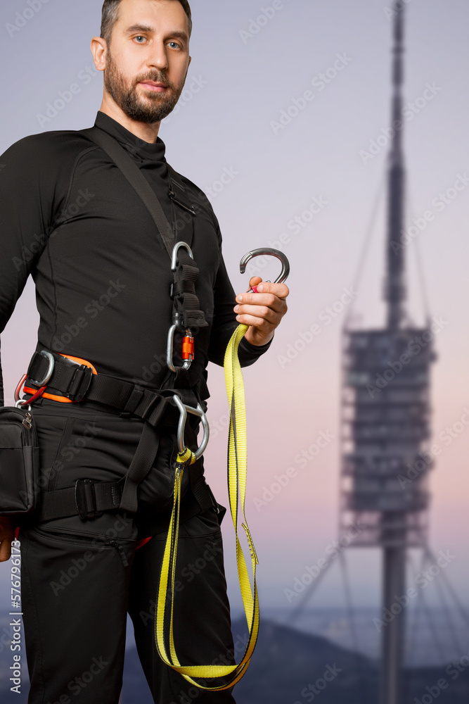 A man in a belay system for work at height. Carabiners, straps, safety ropes. Industrial mountaineering, worker, cell phone towers. A man in a belay system for work at height. Carabiners, straps, safety ropes. Industrial mountaineering, worker, cell phone towers.