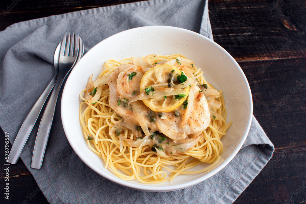 Chicken Piccata Served Over Spaghetti in a Pasta Bowl: Chicken, onions, and lemons in sauce made of garlic and white wine Chicken Piccata Served Over Spaghetti in a Pasta Bowl: Chicken, onions, and lemons in sauce made of garlic and white wine