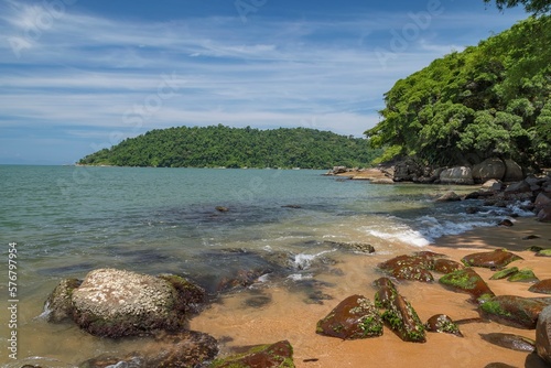 Natural landscape of Prainha in Paraty, Brazil. Sea in shades of turquoise blue, stones, strip of sand and blue sky with white clouds. In the background, the island of Araújo. photo