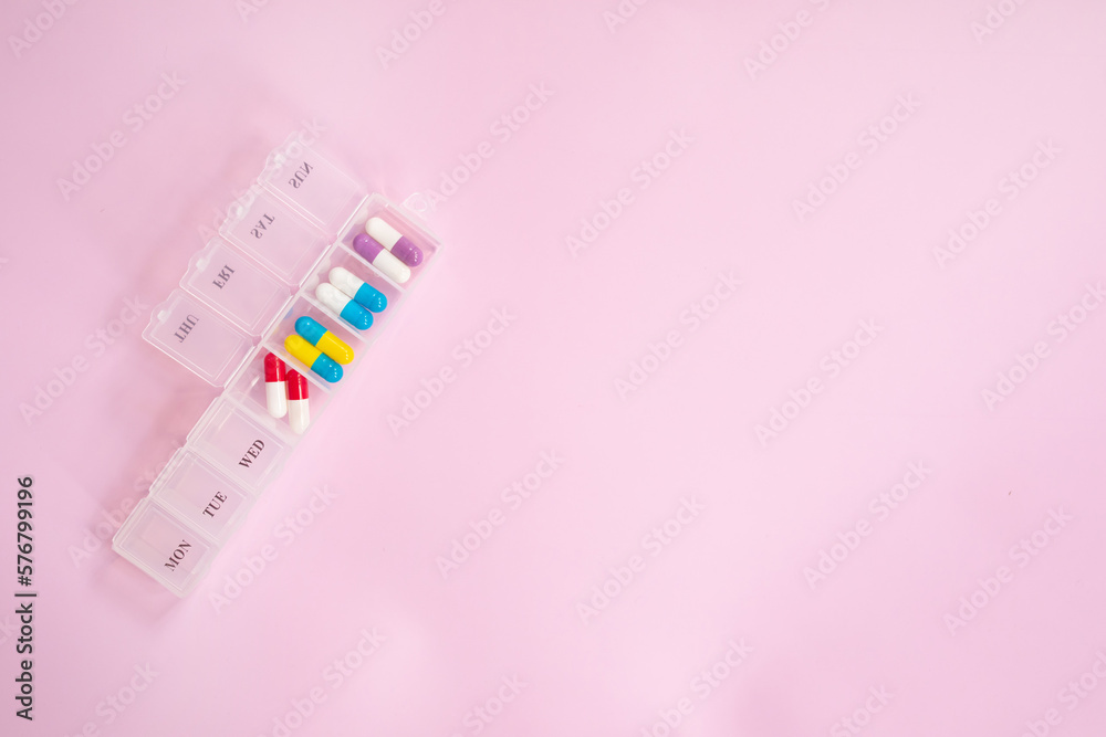 Pill box daily take a medicine, with colorful of pills, tablets, and capsules. Drugs use for treatment and cure the disease on pink background. Medicine concept. 