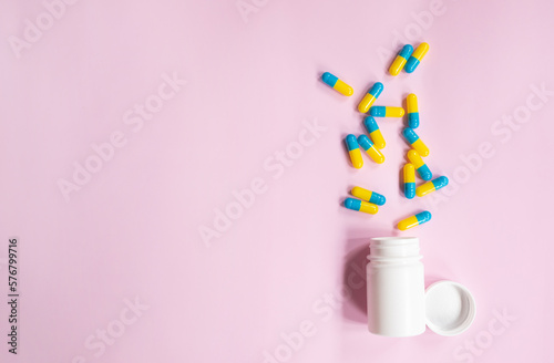 Capsule pills spread out of white plastic drug bottle on pink background. Pharmacy banner. Online pharmacy. Painkiller medicine and antibiotic drug resistance concept.