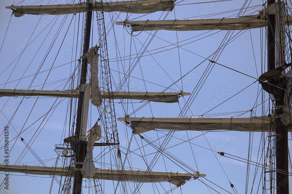 Masts, ropes, sails, ladder and hauled in sails of a historic sailing ship with a blue sky Masts, ropes, sails, ladder and hauled in sails of a historic sailing ship with a blue sky