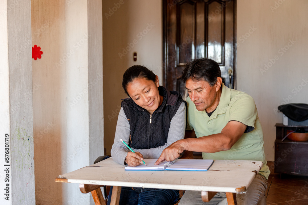 Hispanic adult couple studying together - Mayan teacher teaching senior how to write - couple budgeting at home Hispanic adult couple studying together - Mayan teacher teaching senior how to write - couple budgeting at home