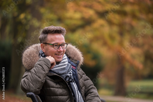 Caucasian man sitting on a bench in a park during autumn looking into the scenery
