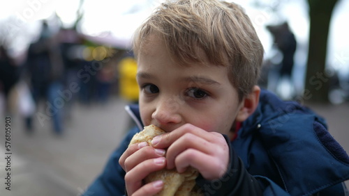 Small boy eating pancake outside in city street during winter season. Hungry child eating food during december festivities