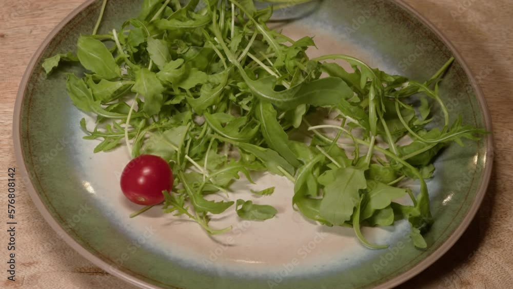 Slow motion fresh cherry tomatoes falling on ceramic plate with mixed salad leaves. Cherry tomato falling down in fresh salad, bouncing. Vegetarian food, organic food. Tasty salad. Slow motion.