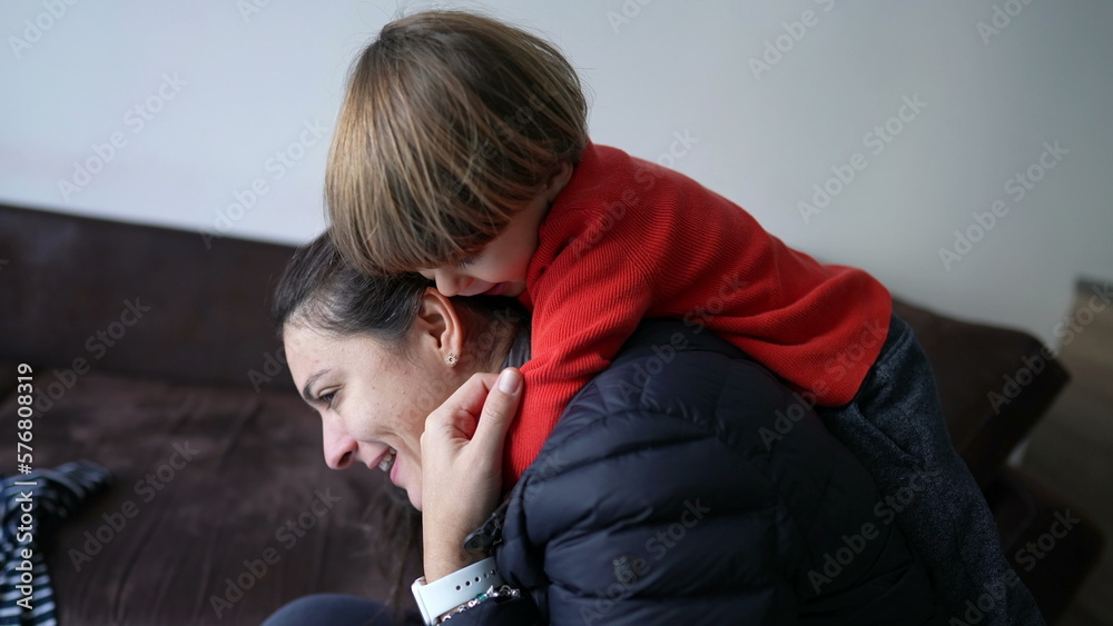 Fototapeta premium Child embracing mother back. Little boy jumping on parent surprise. Authentic real life love relationship