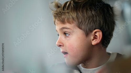 Candid thoughtful young boy closeup face. One pensive child thinking while sitting at lunch table eating meal