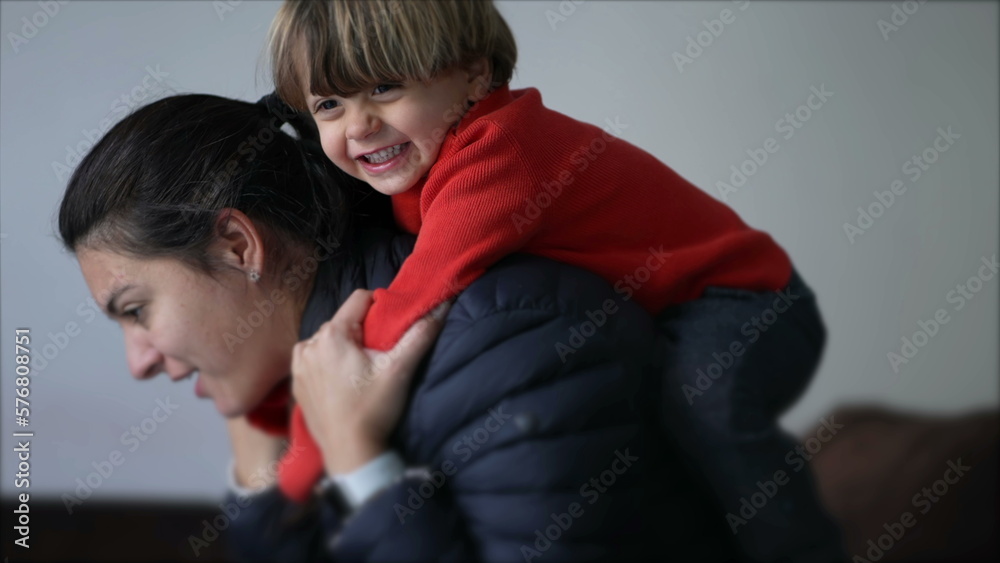 Little boy jumping on mother back. Authentic real life parent and child relationship laughing and smiling. Mom and kid embrace Little boy jumping on mother back. Authentic real life parent and child relationship laughing and smiling. Mom and kid embrace