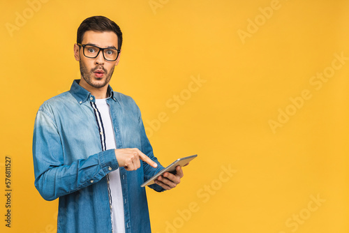 Amazed shocked happy bearded man using digital tablet looking shocked about social media news, astonished man shopper consumer surprised excited by online win isolated over yellow background.